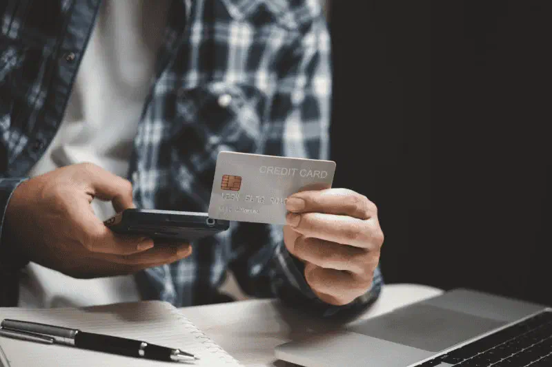 A parent holding a credit card beside a laptop while paying for a program